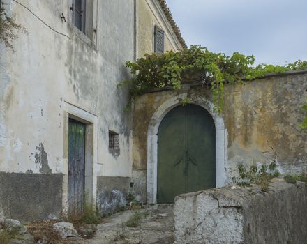Shabby old house with flaking facade and green door at narrow street and stairs, vintage look, Corfu Greece.