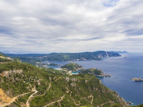 View at zigzag road, hills cllifs, forest and turquoise blue sea at Paleokastritsa bay from the view point at mediavel castle Angelokastro, summer clody day, Corfu, Greece.