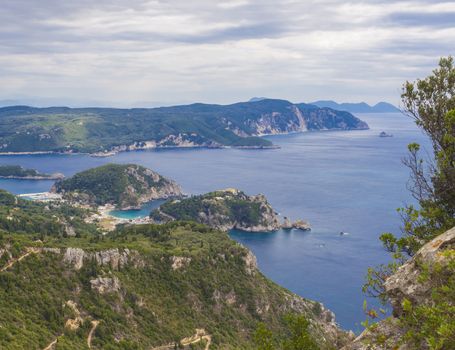 View at zigzag road, hills cllifs, forest and turquoise blue sea at Paleokastritsa bay from the view point at mediavel castle Angelokastro, summer clody day, Corfu, Greece.