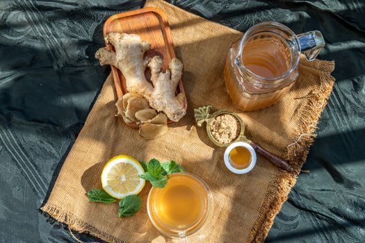 Hot Ginger juice with lemon and mint, root and slices of ginger Served with brown sugar and honey on sackcloth background. Hot ginger juice can helps warming body, Healthy Drink.