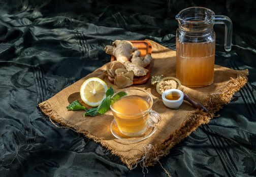 Hot Ginger juice with lemon and mint, root and slices of ginger Served with brown sugar and honey on sackcloth background. Hot ginger juice can helps warming body, Healthy Drink.