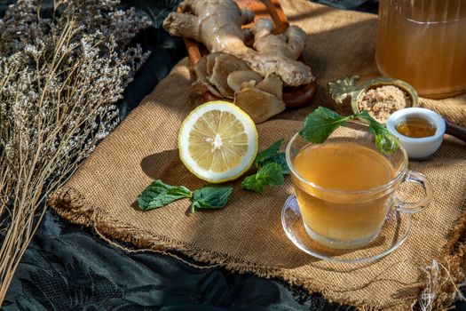 Hot Ginger juice with lemon and mint, root and slices of ginger Served with brown sugar and honey on sackcloth background. Hot ginger juice can helps warming body, Healthy Drink.