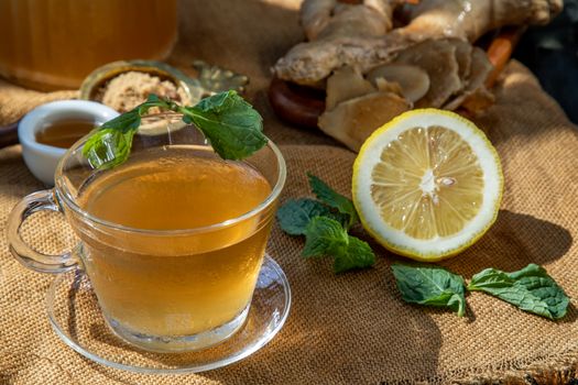 Hot Ginger juice with lemon and mint, root and slices of ginger Served with brown sugar and honey on sackcloth background. Hot ginger juice can helps warming body, Healthy Drink.