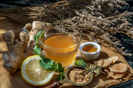 Hot Ginger juice with lemon and mint, root and slices of ginger Served with brown sugar and honey on sackcloth background. Hot ginger juice can helps warming body, Healthy Drink.