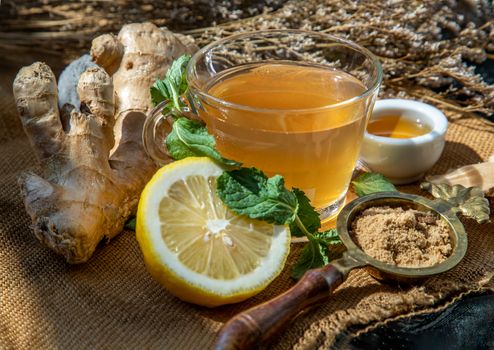Hot Ginger juice with lemon and mint, root and slices of ginger Served with brown sugar and honey on sackcloth background. Hot ginger juice can helps warming body, Healthy Drink.