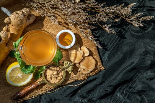 Hot Ginger juice with lemon and mint, root and slices of ginger Served with brown sugar and honey on sackcloth background. Hot ginger juice can helps warming body, Healthy Drink.