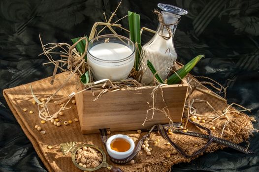 Soy products : A glass of Homemade soy milk and grains (soybeans) in wooden box Served with brown sugar and honey with lighting in the morning. Alternative milk concept, Selective focus, Copy space.