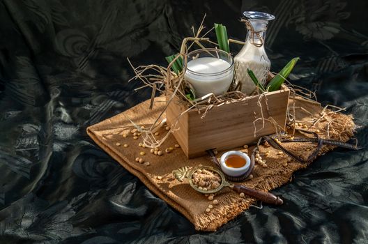Soy products : A glass of Homemade soy milk and grains (soybeans) in wooden box Served with brown sugar and honey with lighting in the morning. Alternative milk concept, Selective focus, Copy space.