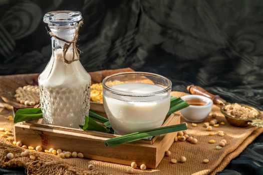 Soy products : A glass of Homemade soy milk and grains (soybeans) in wooden tray Served with brown sugar and honey with lighting in the morning. Alternative milk concept, Front view, Selective focus, Copy space.