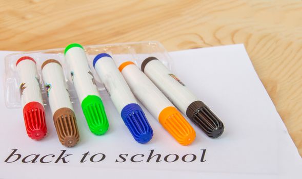 A white sheet of paper with the inscription back to school, colorful markers for drawing, the concept of education.
