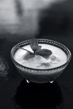 Close up of raw organic curd in a glass bowl along with mint leaf on the top for decoration on wooden surface.