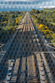 Train tracks located between the mountains, seen from the bridge through the gate. Depth and path concept.