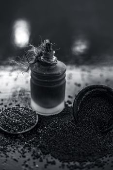 Raw organic herbal spice Mustard seeds or sarso or rai or Brassica nigra, in a clay bowl on wooden surface with its extracted essential oil in a transparent glass bottle.