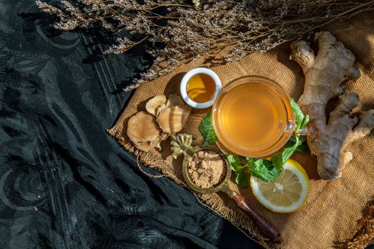 Hot Ginger juice with lemon and mint, root and slices of ginger Served with brown sugar and honey on sackcloth background. Hot ginger juice can helps warming body, Healthy Drink.