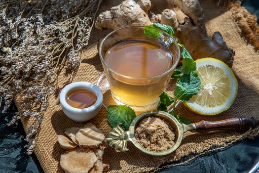 Hot Ginger juice with lemon and mint, root and slices of ginger Served with brown sugar and honey on sackcloth background. Hot ginger juice can helps warming body, Healthy Drink.
