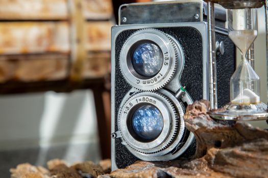 Vintage two lens photo camera with Hourglass on wooden background. An idea of old camera and memory, time Nostalgia.