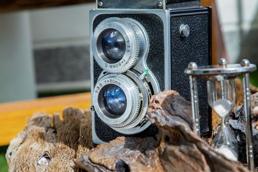 Vintage two lens photo camera with Hourglass on wooden background. An idea of old camera and memory, time Nostalgia.