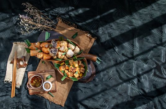 Many vegetarian food : Fried taro rolls (Taro Guangjian) and Deep fried spring rolls, Fried tofu, Fried radish, Fried taro and black beans (Zhu jiao quan or Fried taro cakes) Served with spicy sweet sauce and roasted crushed peanuts with wooden chopsticks on wooden plate. Selective focus.