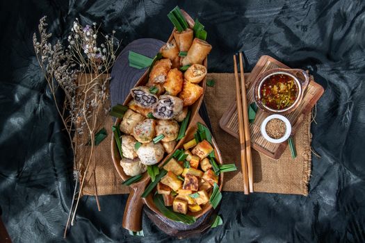 Many vegetarian food : Fried taro rolls (Taro Guangjian) and Deep fried spring rolls, Fried tofu, Fried radish, Fried taro and black beans (Zhu jiao quan or Fried taro cakes) Served with spicy sweet sauce and roasted crushed peanuts with wooden chopsticks on wooden plate. Selective focus.