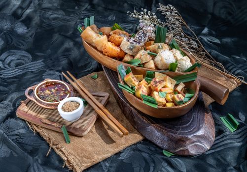 Many vegetarian food : Fried taro rolls (Taro Guangjian) and Deep fried spring rolls, Fried tofu, Fried radish, Fried taro and black beans (Zhu jiao quan or Fried taro cakes) Served with spicy sweet sauce and roasted crushed peanuts with wooden chopsticks on wooden plate. Selective focus.