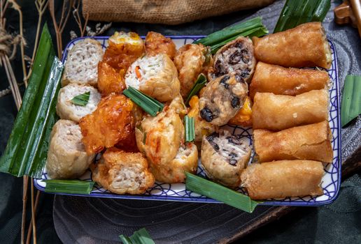 Many vegetarian food : Fried taro rolls (Taro Guangjian) and Deep fried spring rolls, Fried tofu, Fried radish, Fried taro and black beans (Zhu jiao quan or Fried taro cakes) Served with spicy sweet sauce and roasted crushed peanuts with wooden chopsticks on Ceramic dishes. Selective focus.