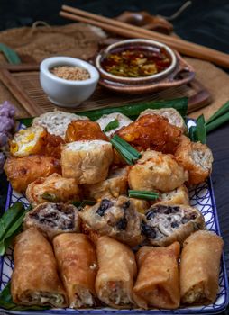 Many vegetarian food : Fried taro rolls (Taro Guangjian) and Deep fried spring rolls, Fried tofu, Fried radish, Fried taro and black beans (Zhu jiao quan or Fried taro cakes) Served with spicy sweet sauce and roasted crushed peanuts with wooden chopsticks on Ceramic dishes. Selective focus.