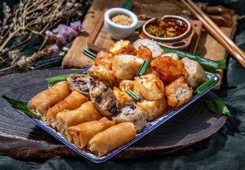 Many vegetarian food : Fried taro rolls (Taro Guangjian) and Deep fried spring rolls, Fried tofu, Fried radish, Fried taro and black beans (Zhu jiao quan or Fried taro cakes) Served with spicy sweet sauce and roasted crushed peanuts with wooden chopsticks on Ceramic dishes. Selective focus.