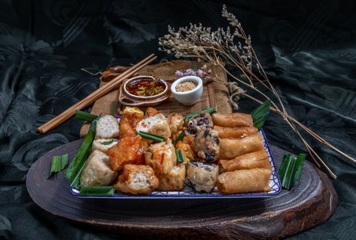 Many vegetarian food : Fried taro rolls (Taro Guangjian) and Deep fried spring rolls, Fried tofu, Fried radish, Fried taro and black beans (Zhu jiao quan or Fried taro cakes) Served with spicy sweet sauce and roasted crushed peanuts with wooden chopsticks on Ceramic dishes. Selective focus.