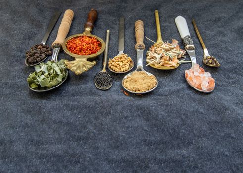 Various teas and dried herbs assortment on spoons in rustic style on balck background. Organic herbal. Selective focus.