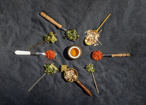 Various teas and dried herbs assortment on spoons in rustic style with honey on balck background. Organic herbal, Selective focus.