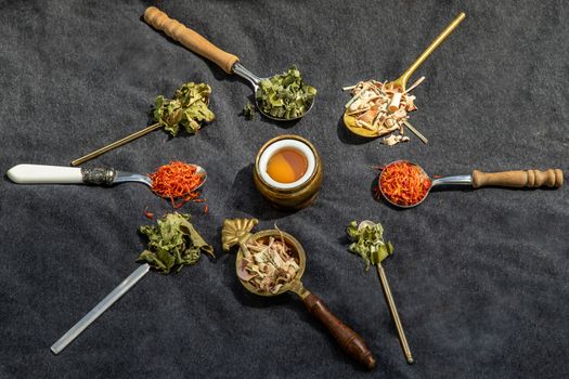 Various teas and dried herbs assortment on spoons in rustic style with honey on balck background. Organic herbal, Selective focus.