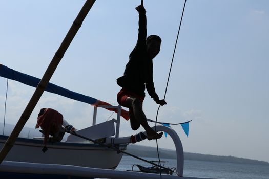 Happy young Indonesian man jumps on the beach. A teenager in a good mood jumps in the air. Sunny tropical day with blue sky.