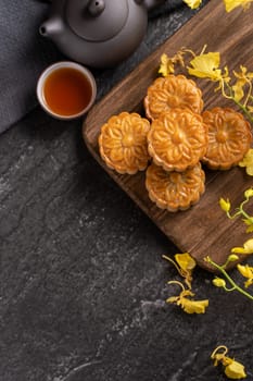 Mooncake, Moon cake for Mid-Autumn Festival, concept of traditional festive food on black slate table with tea and yellow flower, close up, copy space.