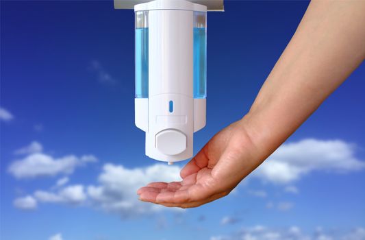 Closeup of Female hand using alcohol gel disinfecting hands. Washing hands using automatic sanitizer dispenser with a blue sky blurred background. 