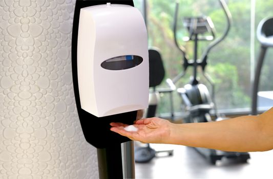 Closeup of Hands under the automatic alcohol dispenser with fitness center background. Fitness gym protection virus concept after Fitness isolation period.