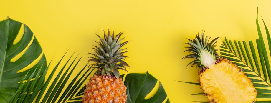 Beautiful pineapple on tropical palm monstera leaves isolated on bright pastel yellow background, top view, flat lay, overhead above summer fruit.