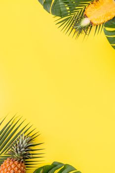 Beautiful pineapple on tropical palm monstera leaves isolated on bright pastel yellow background, top view, flat lay, overhead above summer fruit.