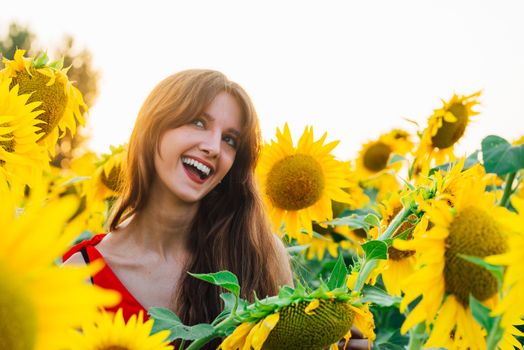 Happy woman with sunflower enjoying nature and laughing on summer sunflower field.