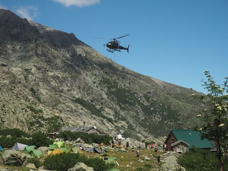 France, Corsica, Corsician Alps, June 19, 2017: helicopter dropping off supplies for mountain camp Refuge de Pietra Piana on famous hiking trail GR20, rocks, tents, tree and blue sky background