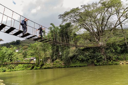 Old walkway footbridge Wooden planks Rope Suspension Bridge crossing river in jungle