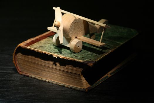 Education concept. Small wooden airplane on old book against dark background