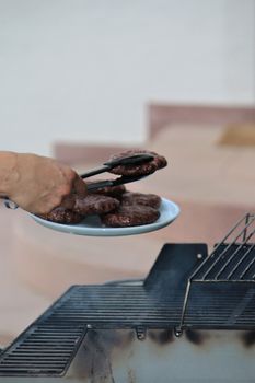 One hand uses a pair of tongs to place burgers on a plate
