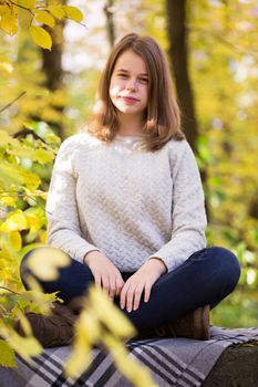 Beautiful teenager girl sitting in autumn garden on the fence , on woolen plaid blanket