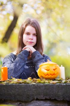 Beautiful teenager girl in autumn garden with halloween pumpkin and candles