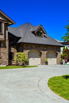 Fragment of luxury house with double garage and concrete driveway in front. Front yard of luxury family house with green lawn and driveway in front on blue sky background