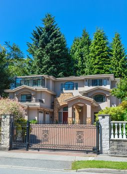 Luxury residential house with double garage and metal gate in front. Beautiful house in suburb of Vancouver on blue sky background