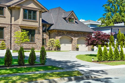 Fragment of luxury house with double garage and concrete driveway in front. Front yard of luxury family house with green lawn and concrete driveway in front on blue sky background