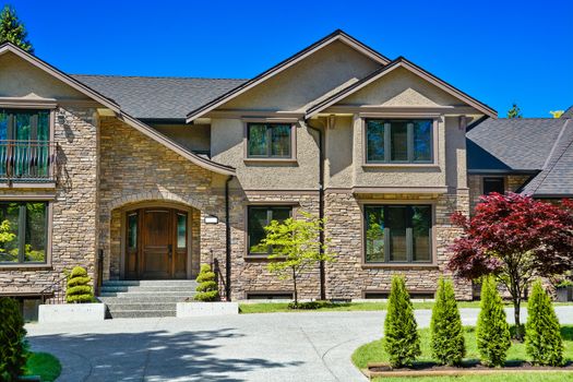 Entrance of luxury family house with green lawn and concrete driveway in front on blue sky background