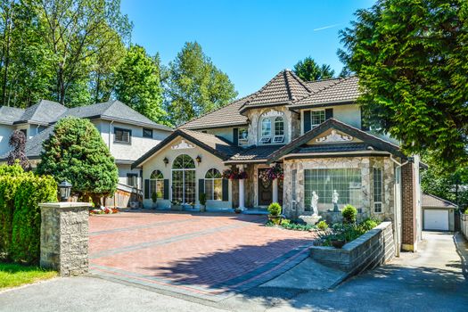 Luxury residential house with garage on back yard and tile paved front yard. Beautiful house in suburb of Vancouver on blue sky background