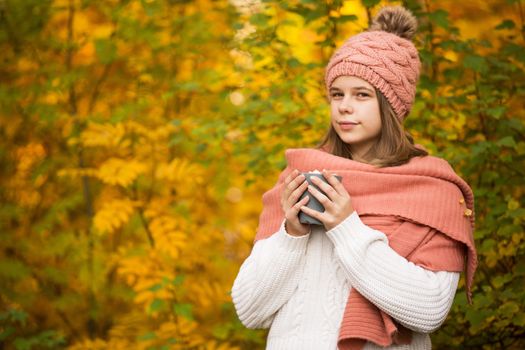 Portrait of pretty nice teenage girl drinking hot cocoa with marshmallows in autumn park